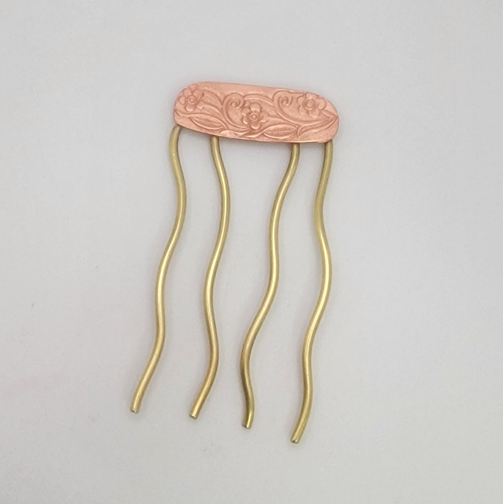 Decorative hair comb with a floral copper top and brass prongs on a light gray background