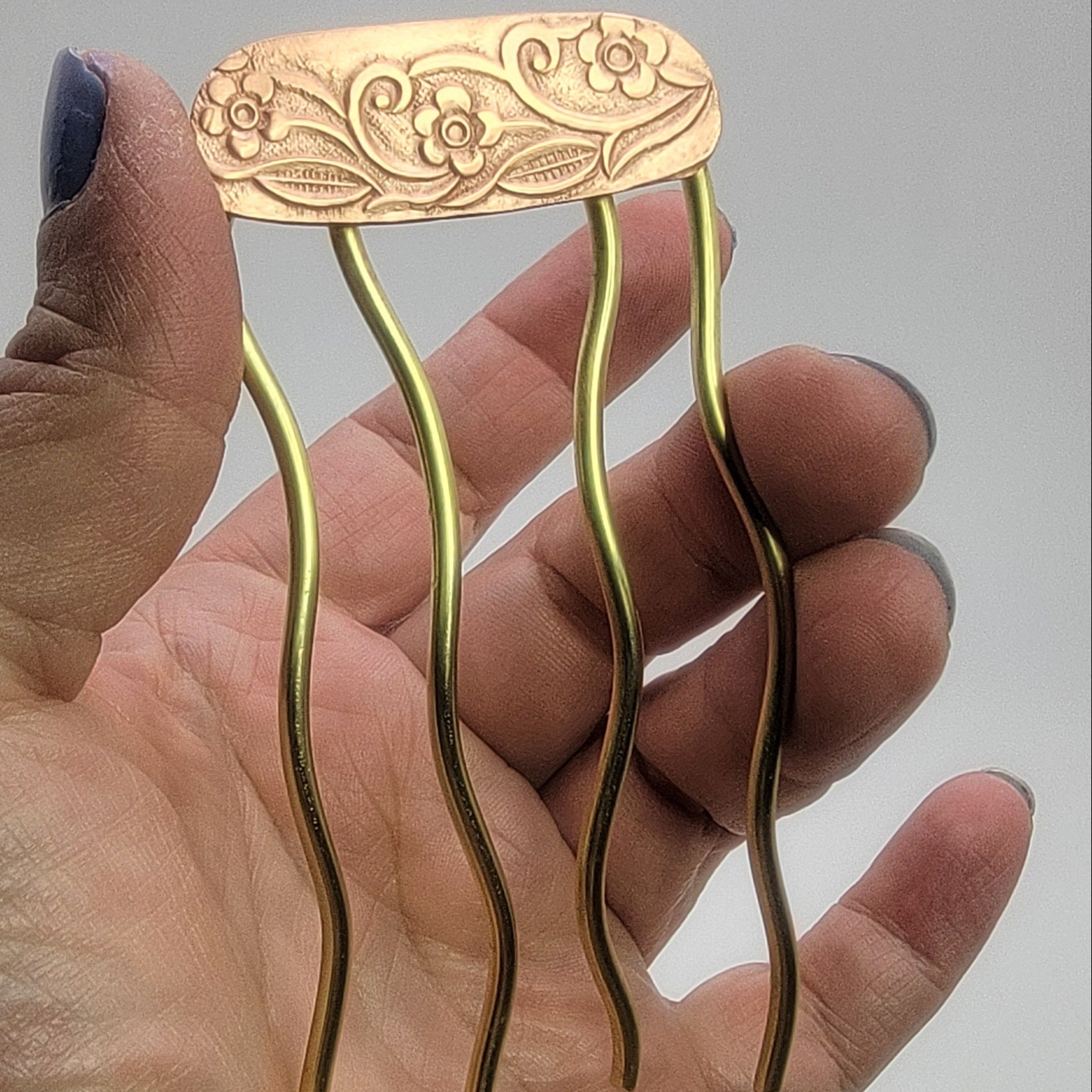 Brass hairpin with decorative top held in a hand against a neutral background