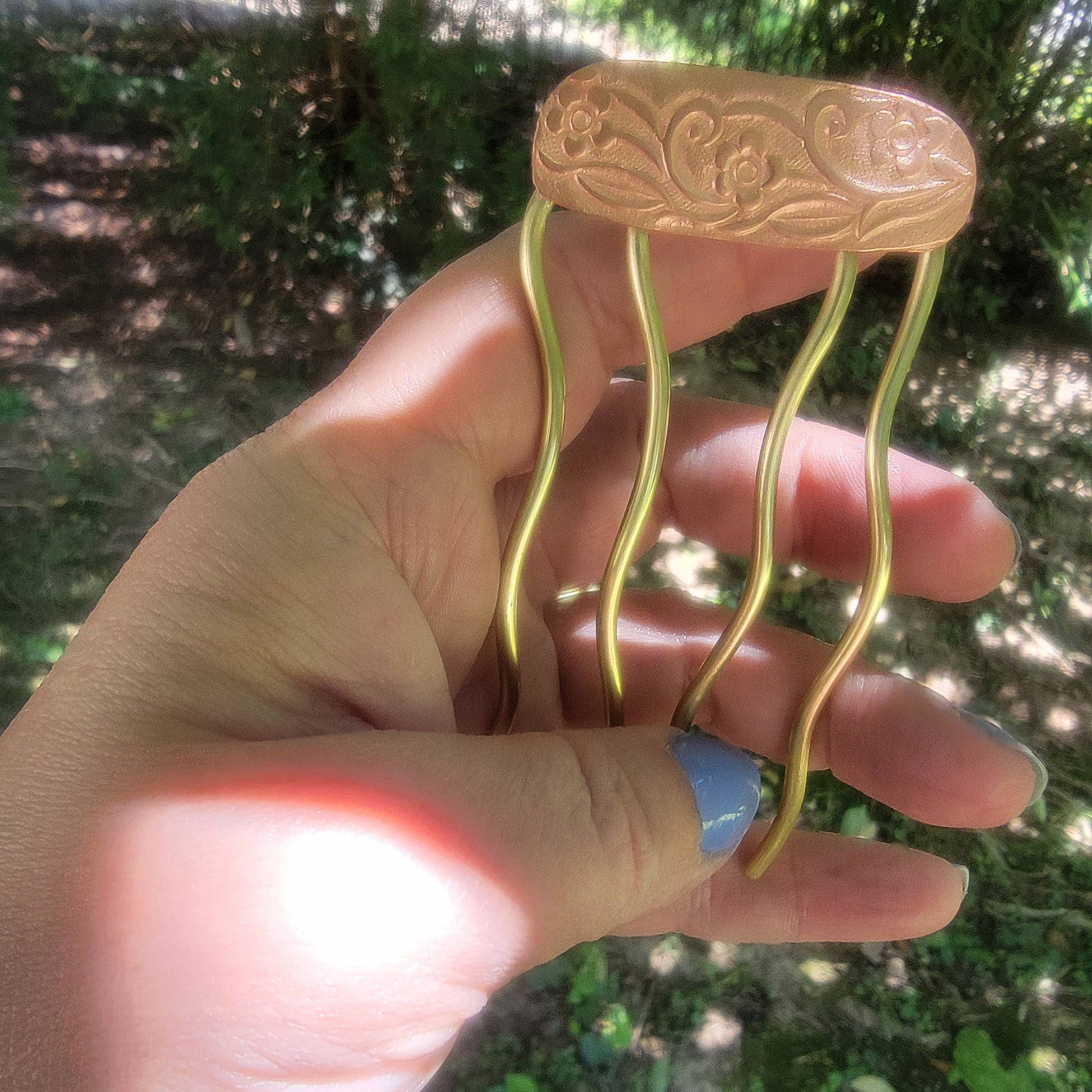 Brass hair fork held by a hand with a blurred green outdoor background