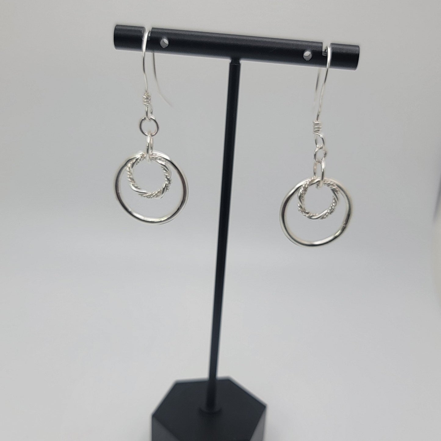Black jewelry display with silver earrings on a white background