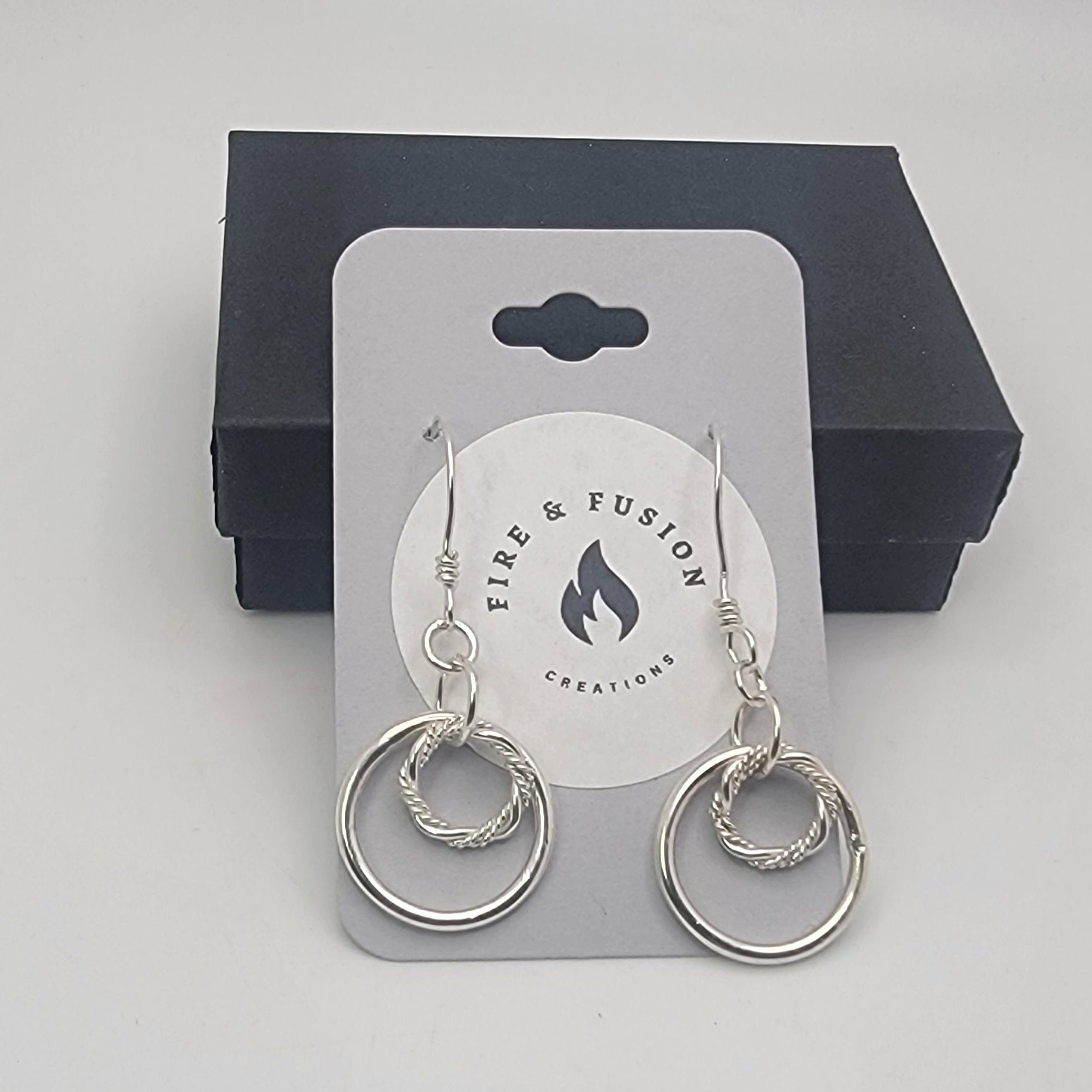 Silver hoop earrings on a Fire & Fusion Creations card with a black box in the background.