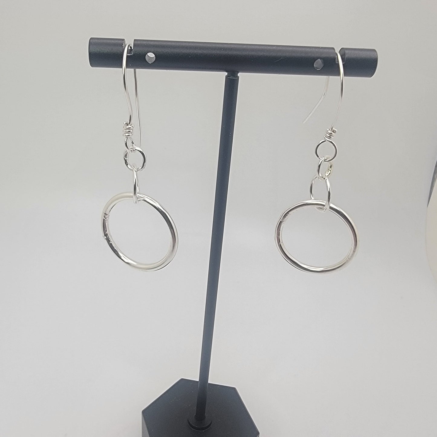 Black earring holder with two silver earrings on a white background