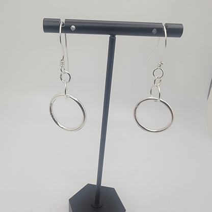 Black earring holder with two silver earrings on a white background