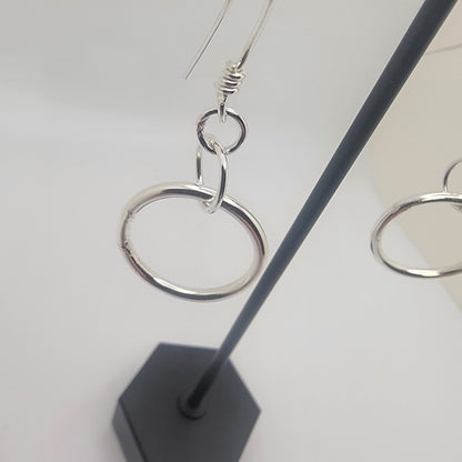 Silver hoop earrings on a stand with a white background