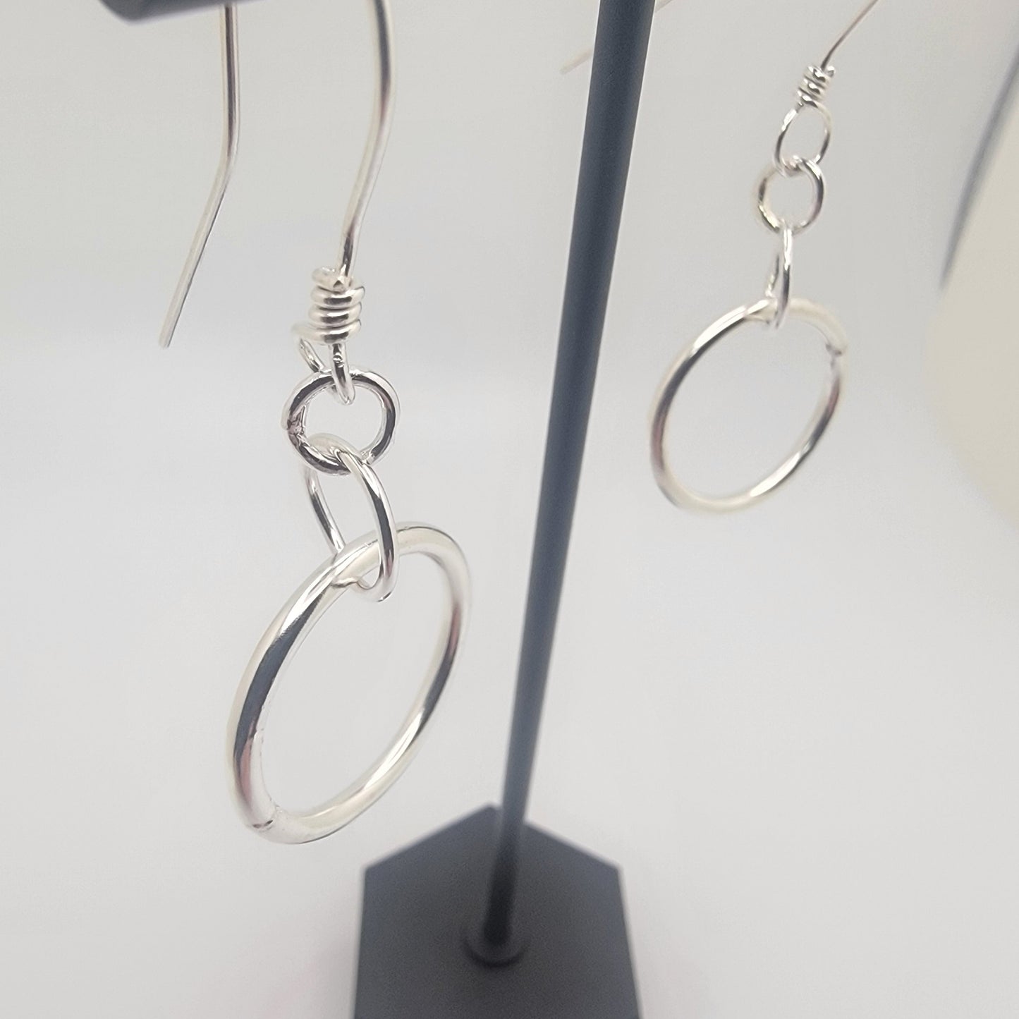Silver hoop earrings on a black stand against a light gray background