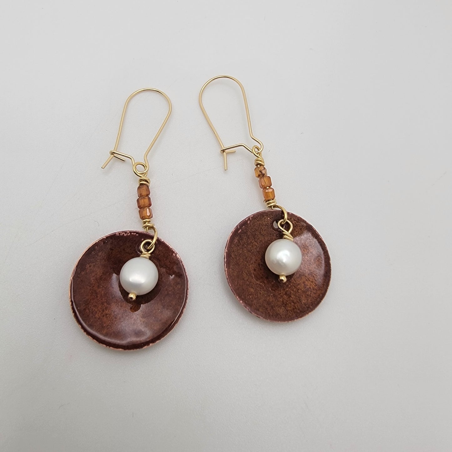 Pair of earrings with brown circular drops and white pearls on a light gray background