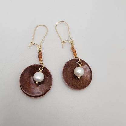 Pair of earrings with brown circular drops and white pearls on a light gray background