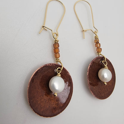 Pair of earrings with brown circular pendants and white pearls on a light gray background