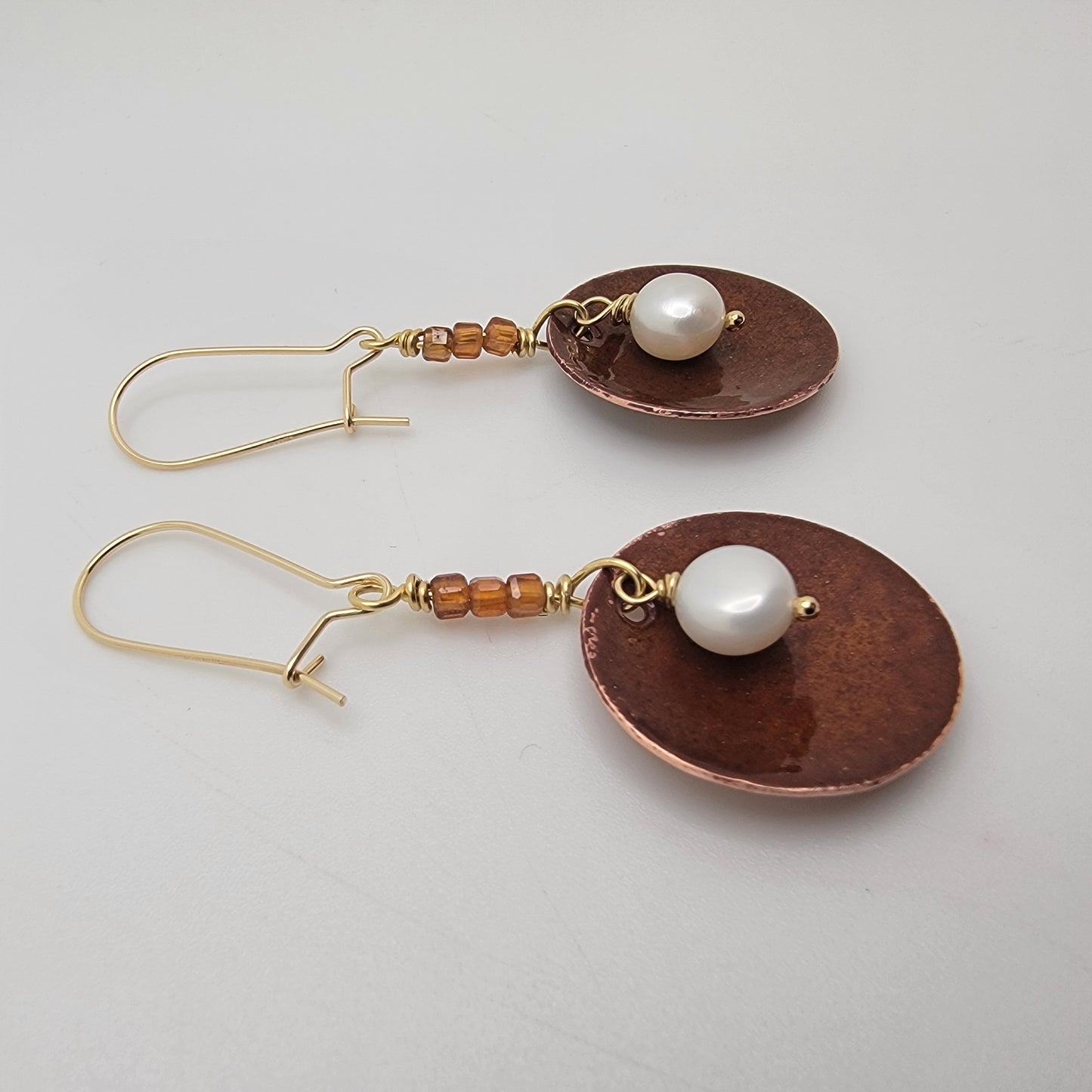 Pair of earrings with copper discs, pearls, and beads on a light gray background