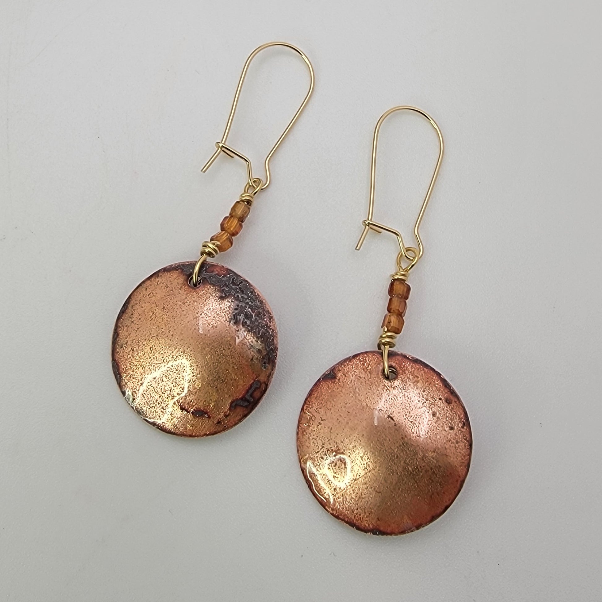 Pair of copper earrings with gold accents on a light gray background