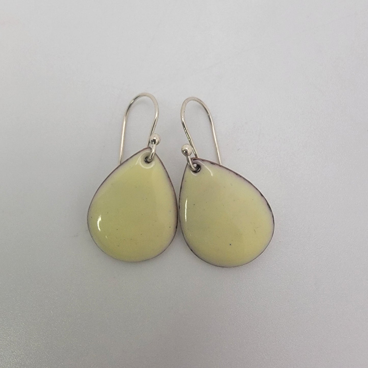 Pair of light yellow teardrop-shaped earrings on a white background