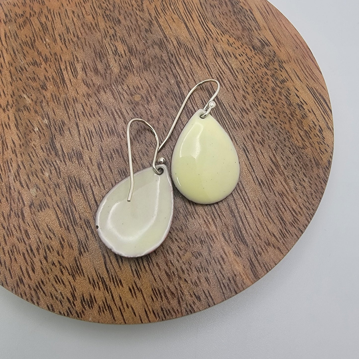 Pair of light yellow teardrop shaped earrings on a wooden round platform.