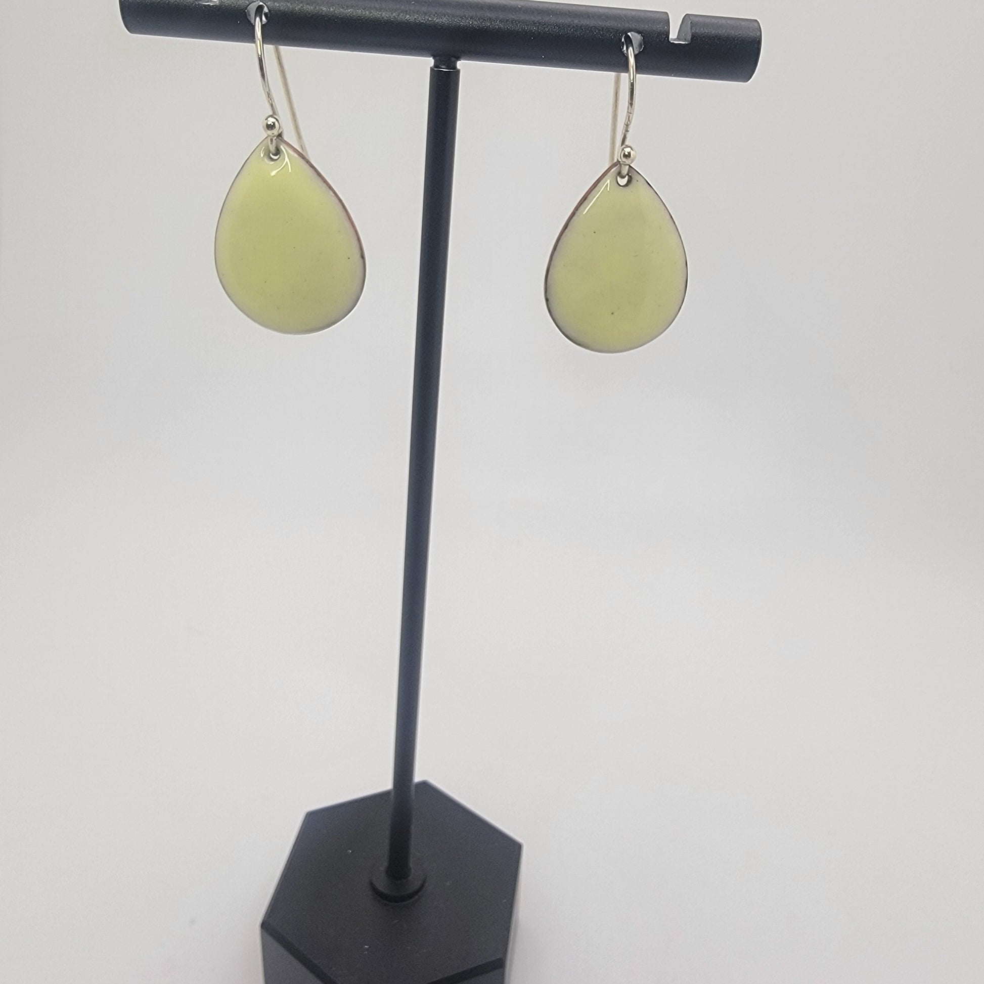 A pair of yellow earrings on a black earring stand on a white background