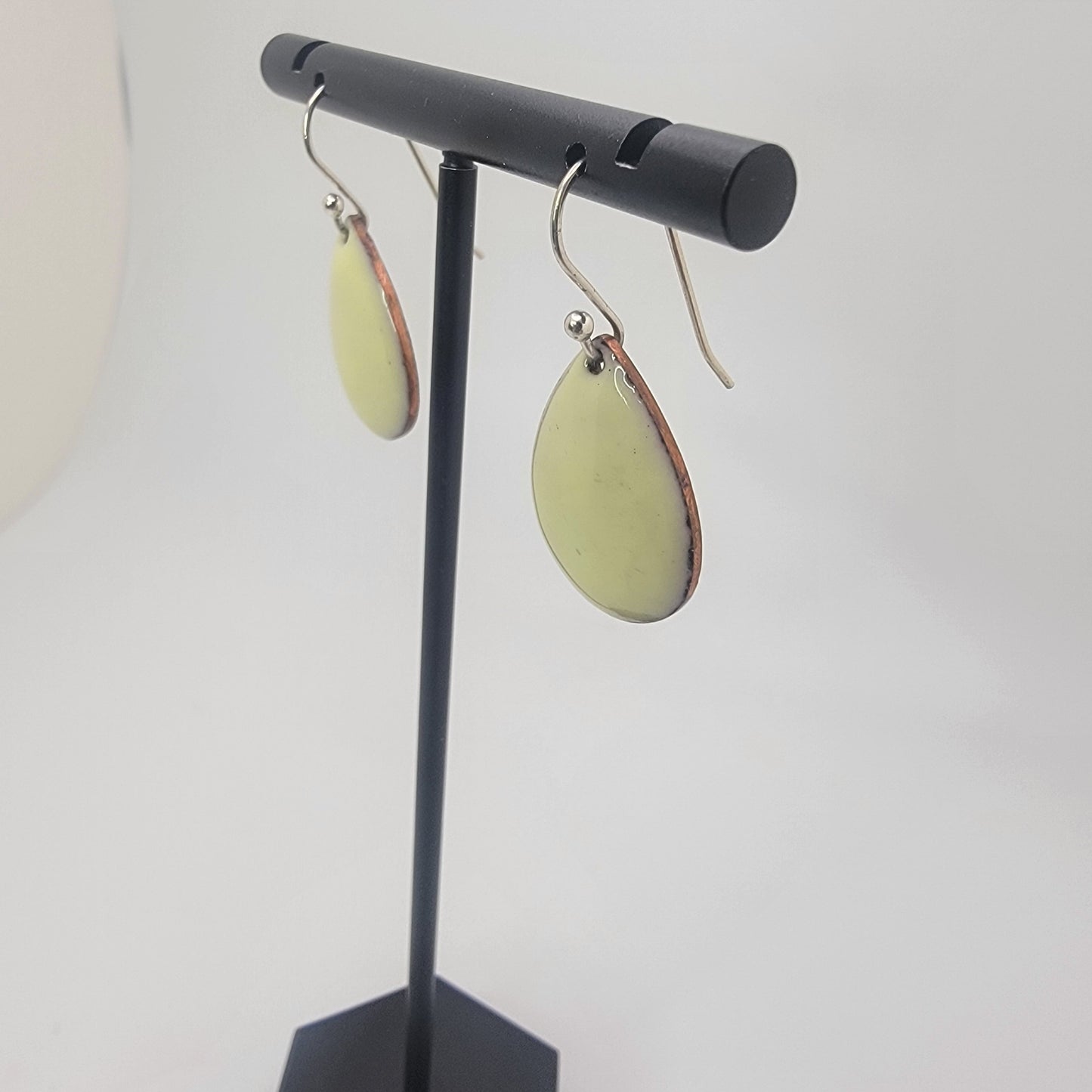 A pair of yellow earrings on a black earring stand on a white background