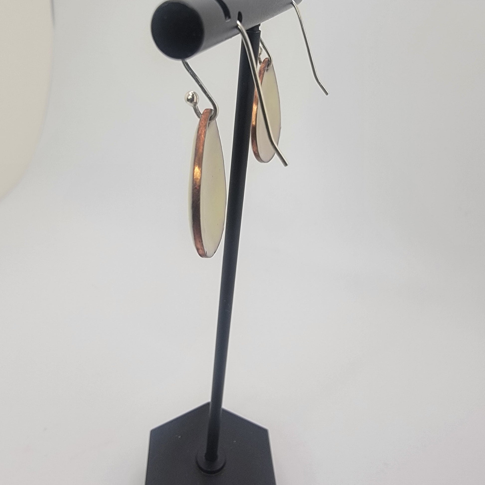 A pair of yellow earrings on a black earring stand on a white background