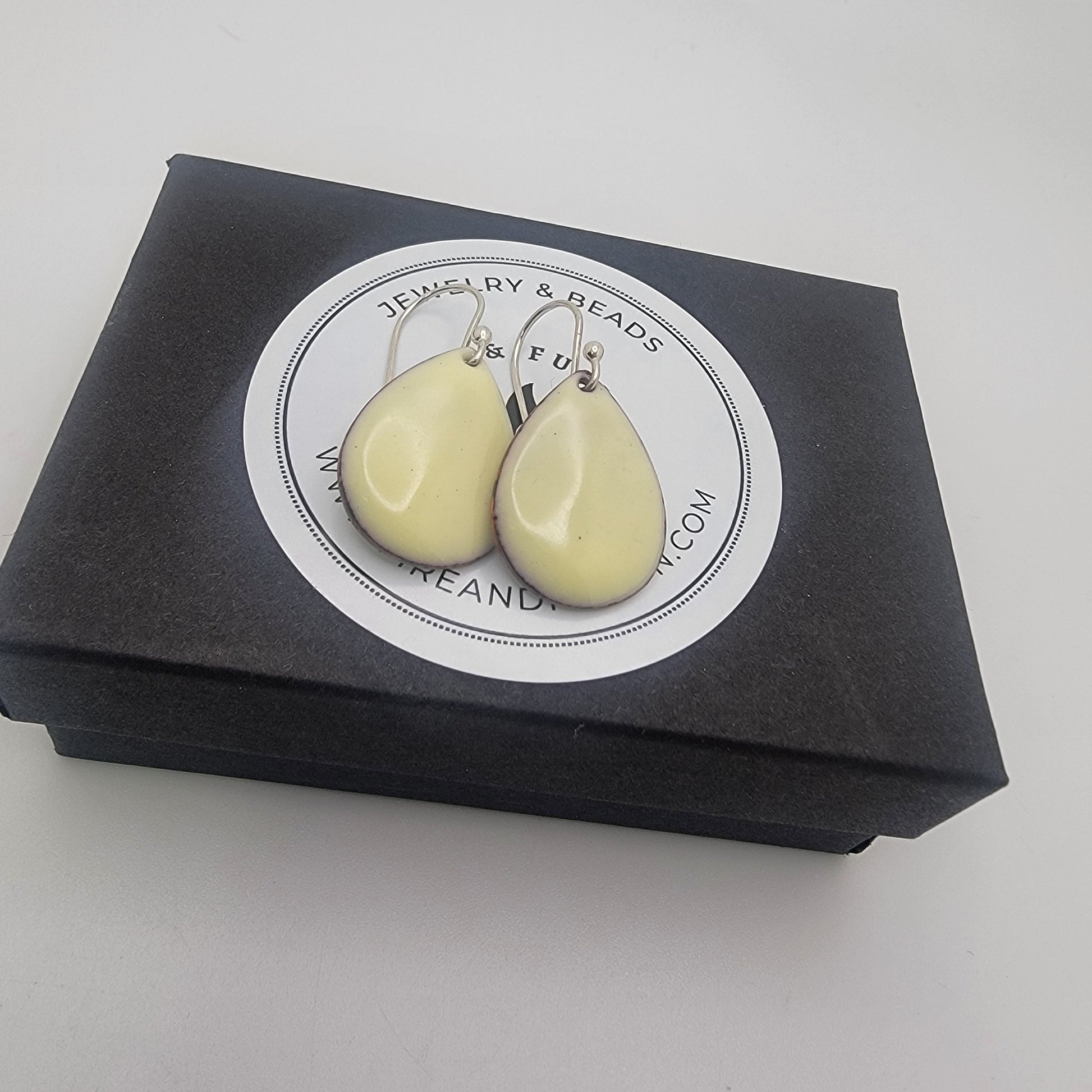 Pair of light yellow teardrop-shaped earrings on a black box with branding.