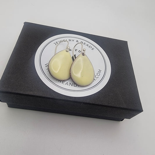 Pair of light yellow teardrop-shaped earrings on a black box with branding.