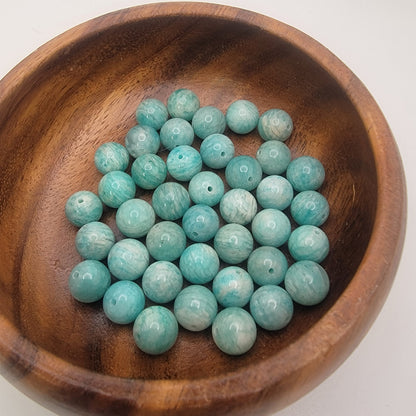 Amazonite beads in a wooden bowl on a white background