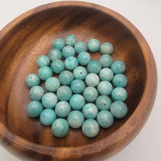 Amazonite beads in a wooden bowl on a white background