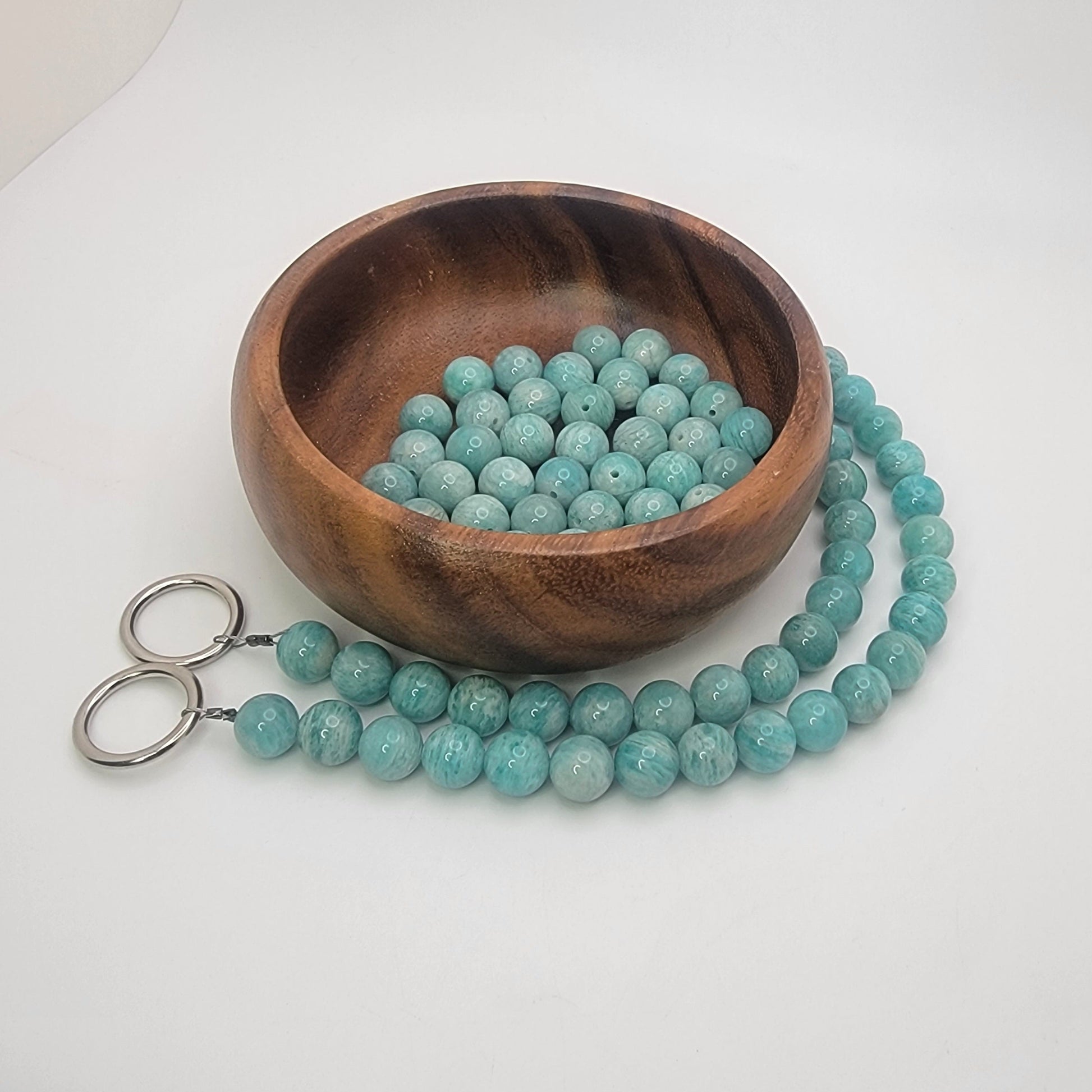 Wooden bowl filled with amazonite beads and a string of beads on a white background