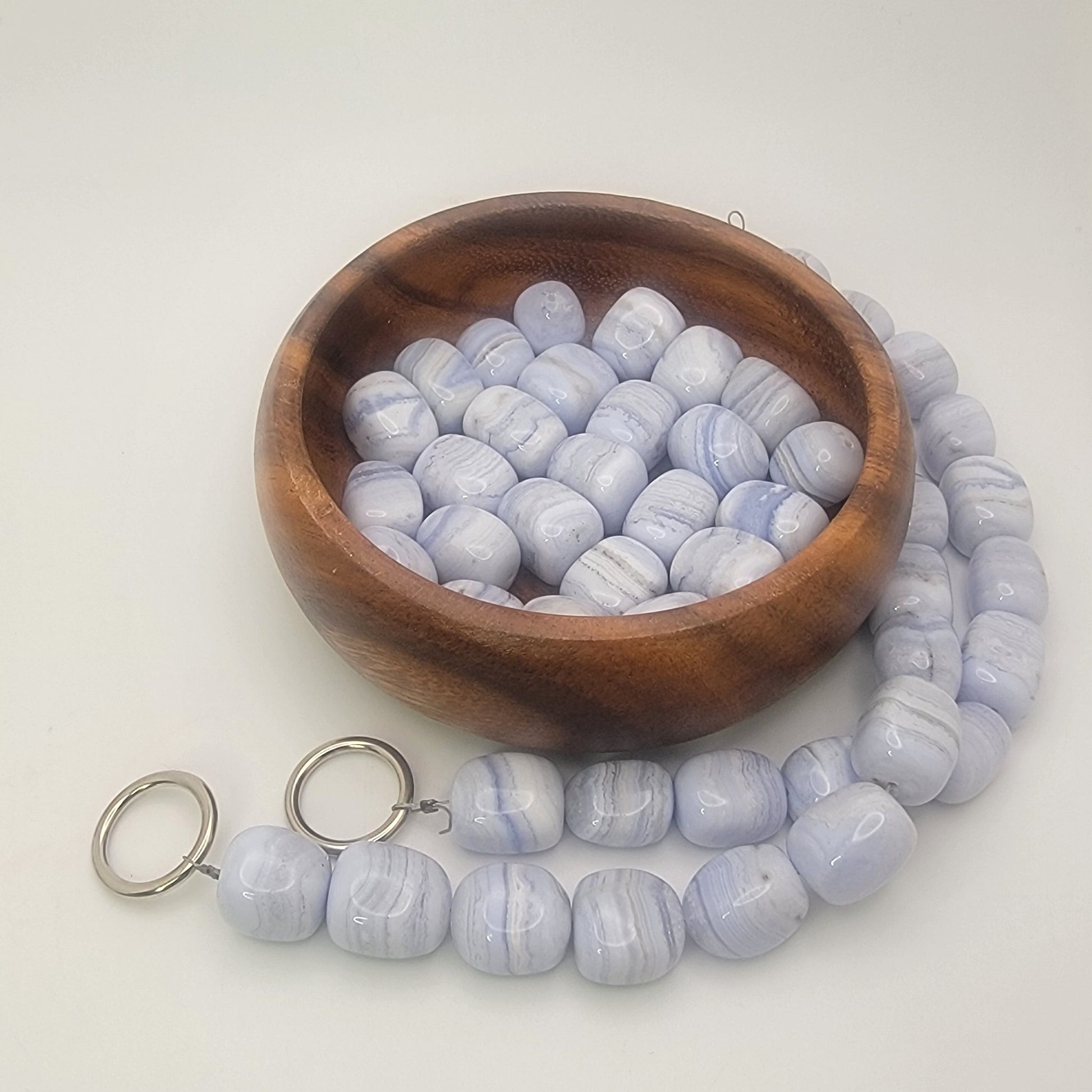 Wooden bowl with blue lace agate beads and a string of beads on a white surface