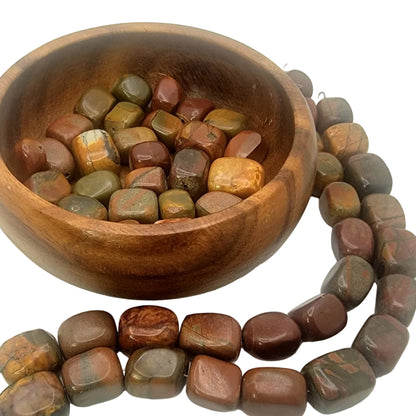 Wooden bowl filled with polished stones next to a string of similar stones on a white background