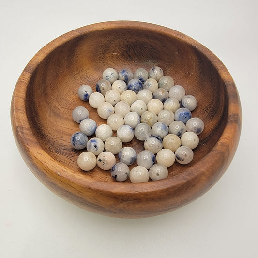Wooden bowl filled with white and blue beads on a light background