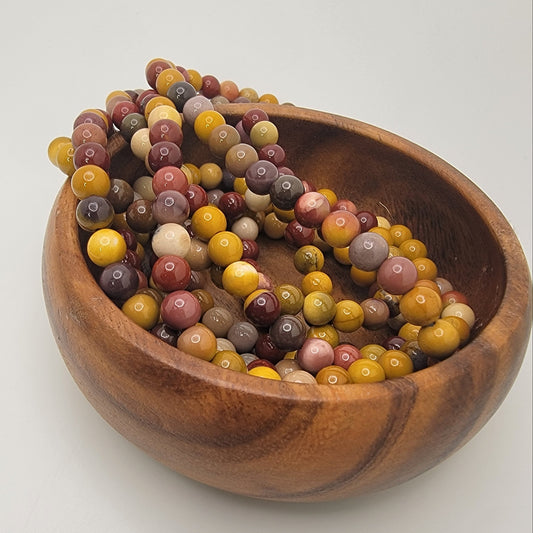 Red and natural color beads in wood bowl on white background