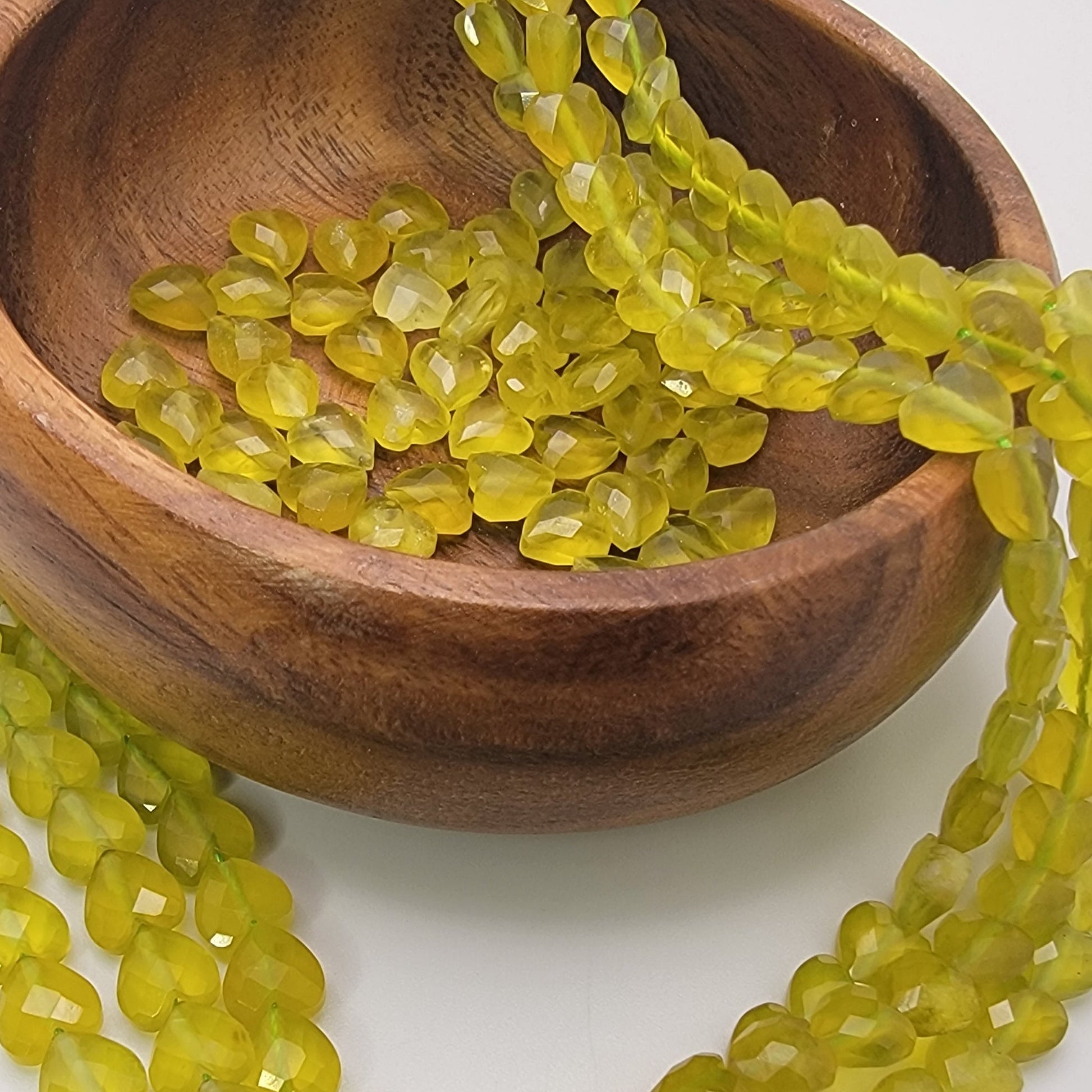 Green heart shaped beads in wood bowl on white background
