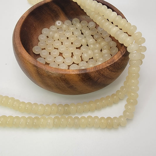 Wooden bowl with a string of pale yellow beads on a white background