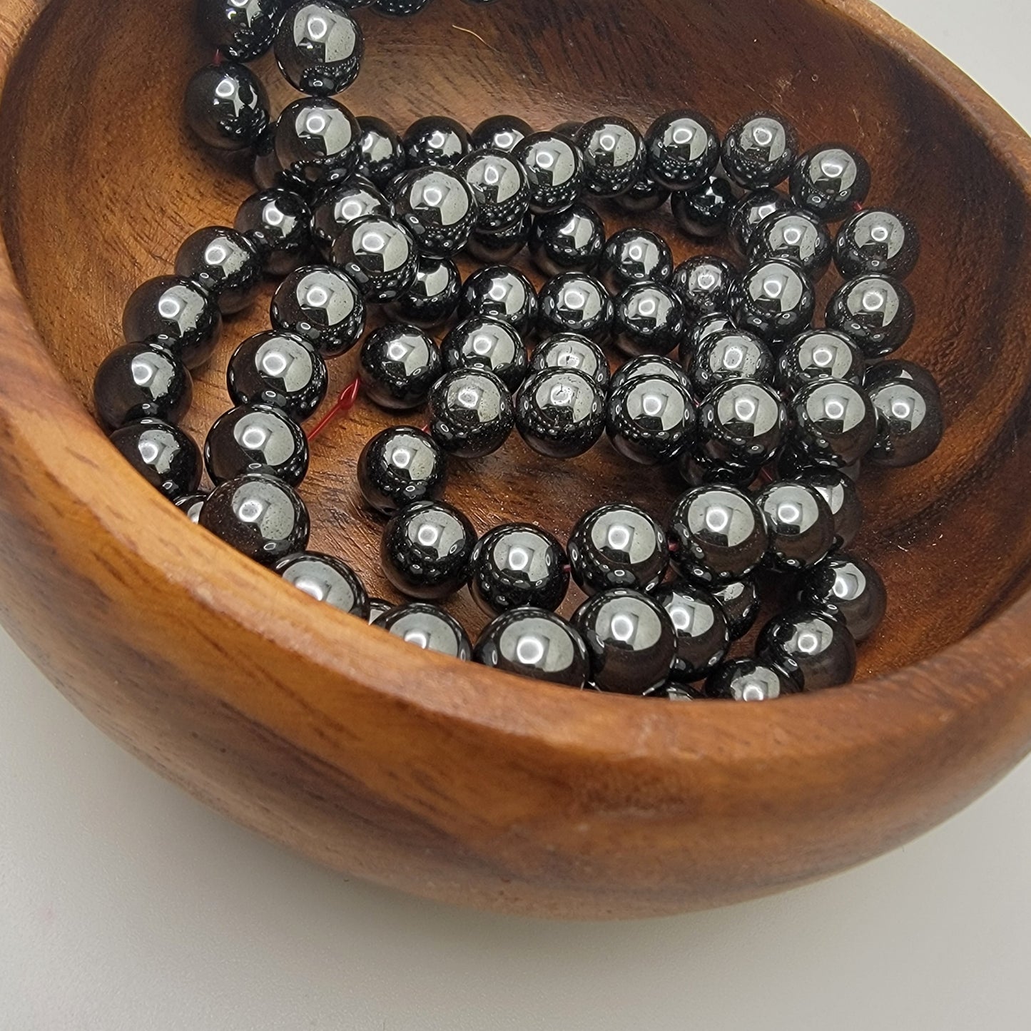 Black beads in a wooden bowl on a white background