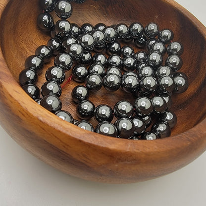 Black beads in a wooden bowl on a white background