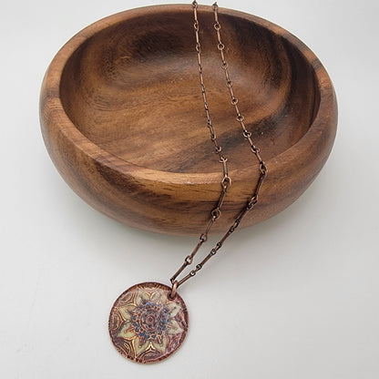 Copper necklace with a decorative mandala pendant on a wooden bowl