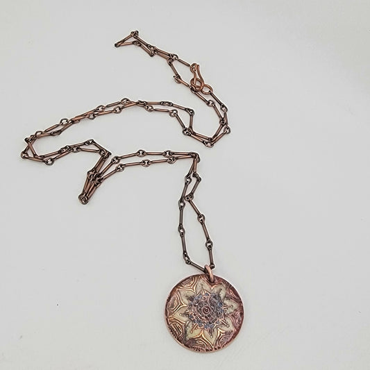 Copper chain necklace with a round, intricately designed mandala pendant on a light gray background