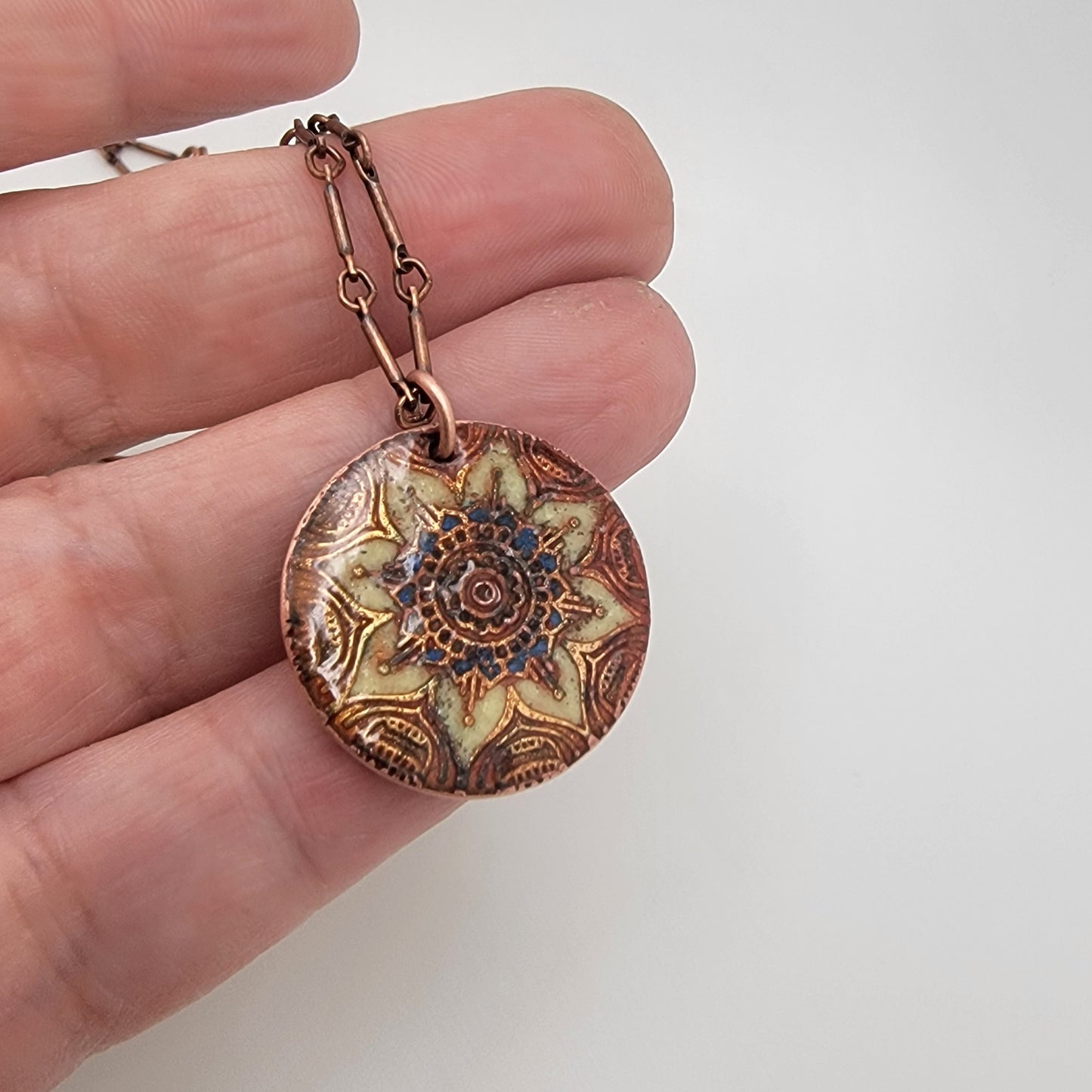 Decorative copper pendant held in a hand against a plain background