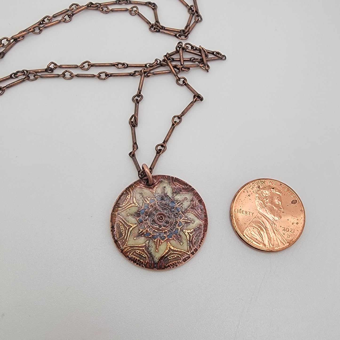 Decorative metal piece with chain next to penny on a light gray background
