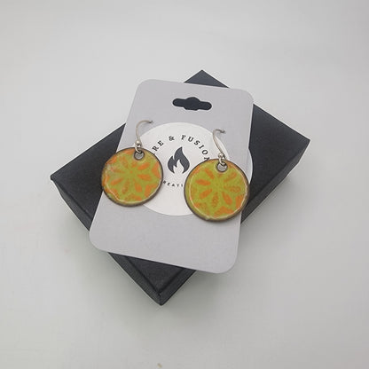 Pair of round earrings with orange and green design on a branded card against a white background