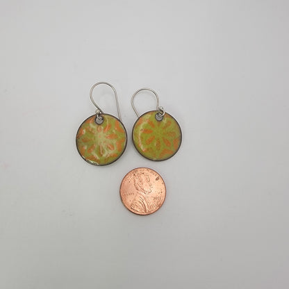 Pair of round earrings with floral design next to a penny on a gray background