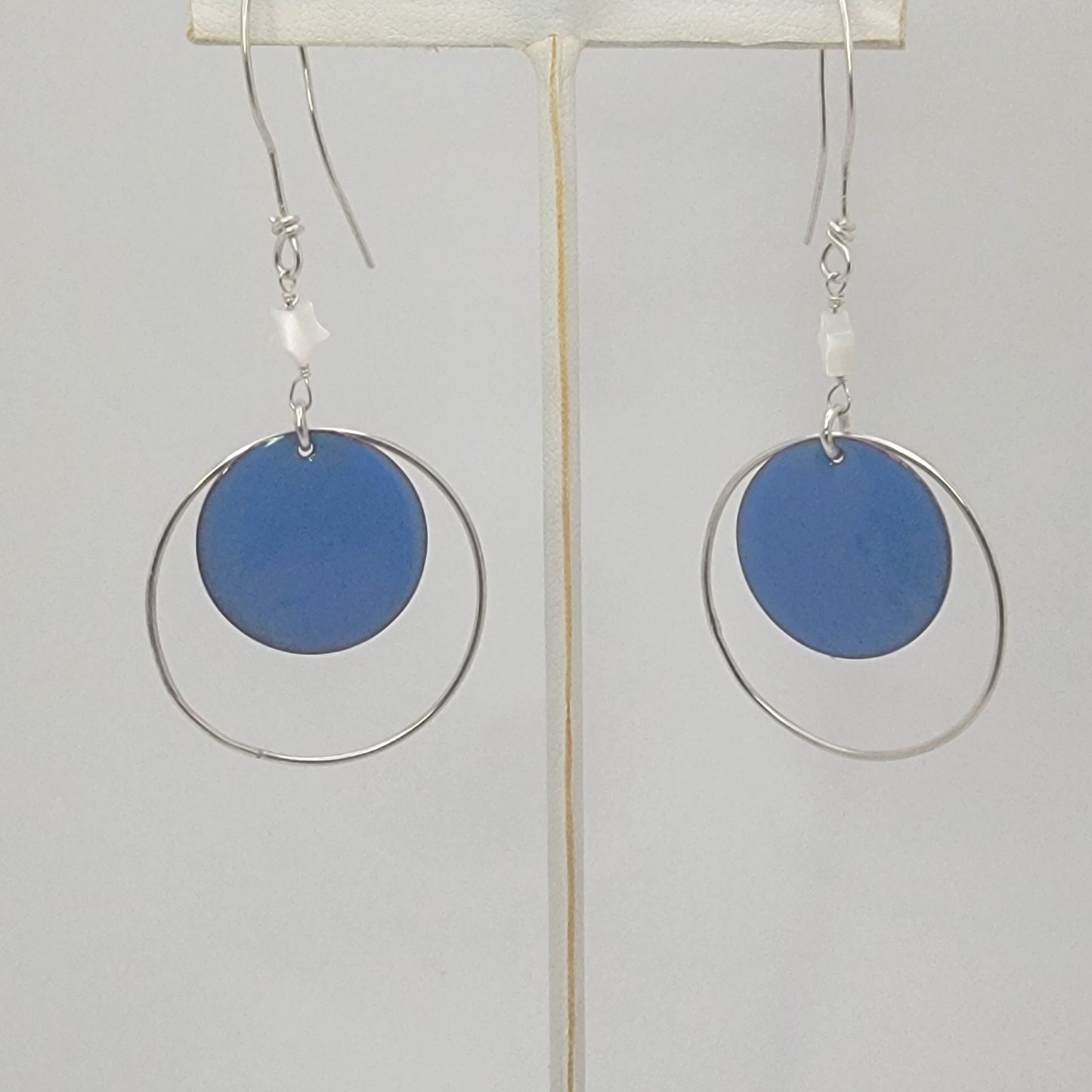 Earrings with blue circular enameled drops and silver loops on a white background