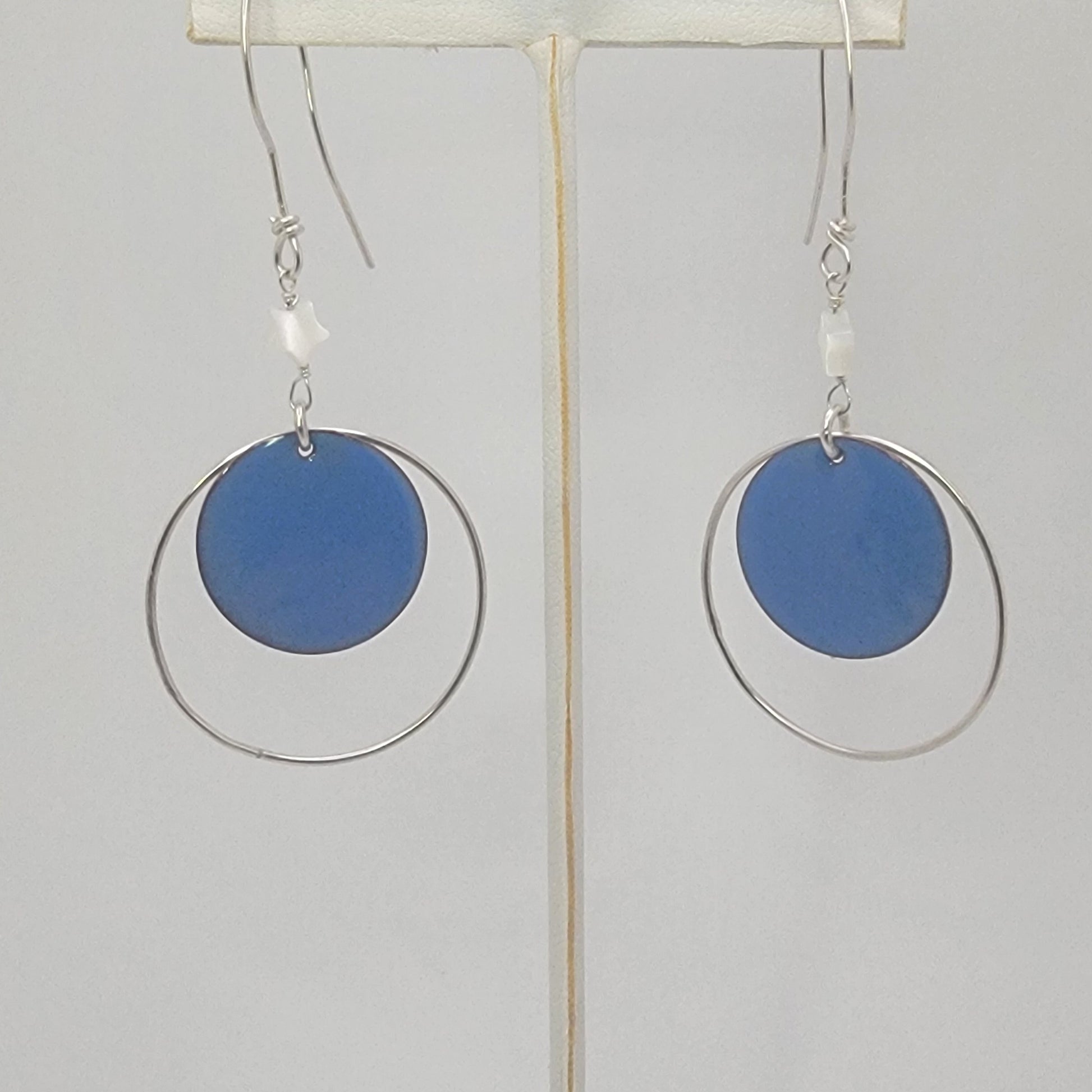 Earrings with blue circular enameled drops and silver loops on a white background