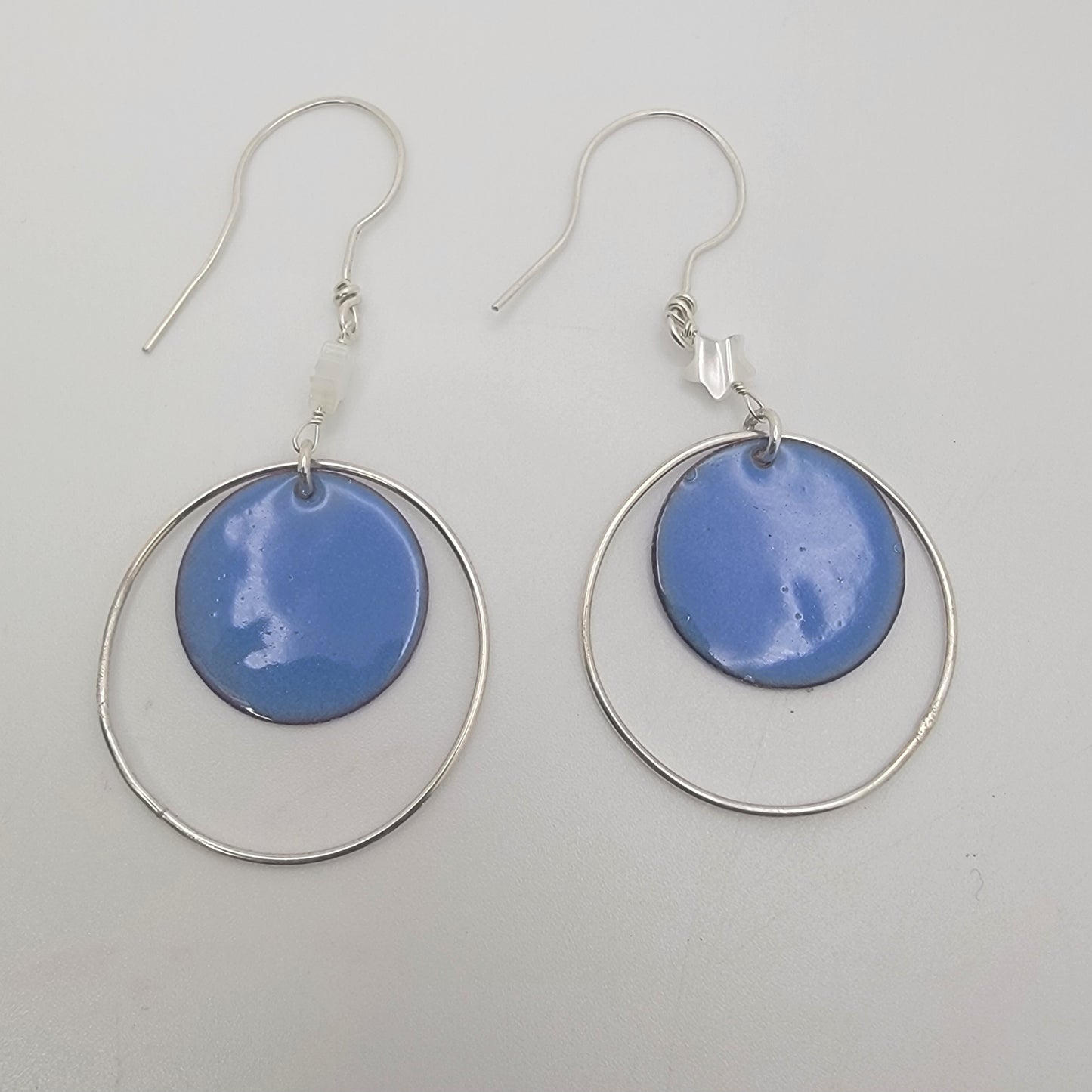 Pair of earrings with blue circular enameled drops and silver loops on a light gray background