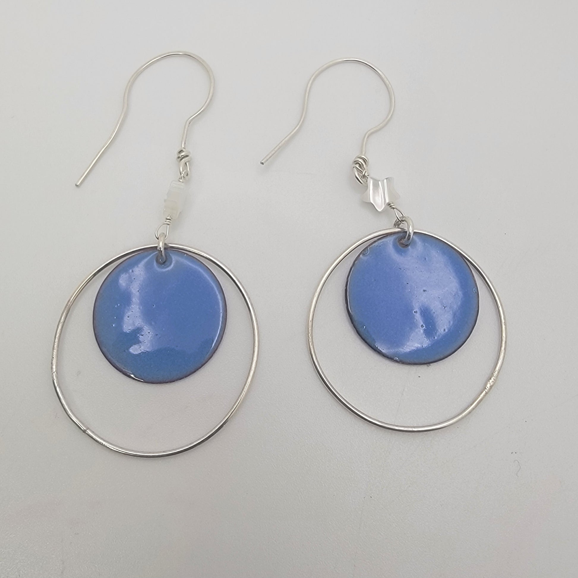 Pair of earrings with blue circular enameled drops and silver loops on a light gray background