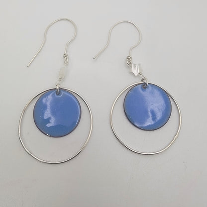 Pair of earrings with blue circular enameled drops and silver loops on a light gray background