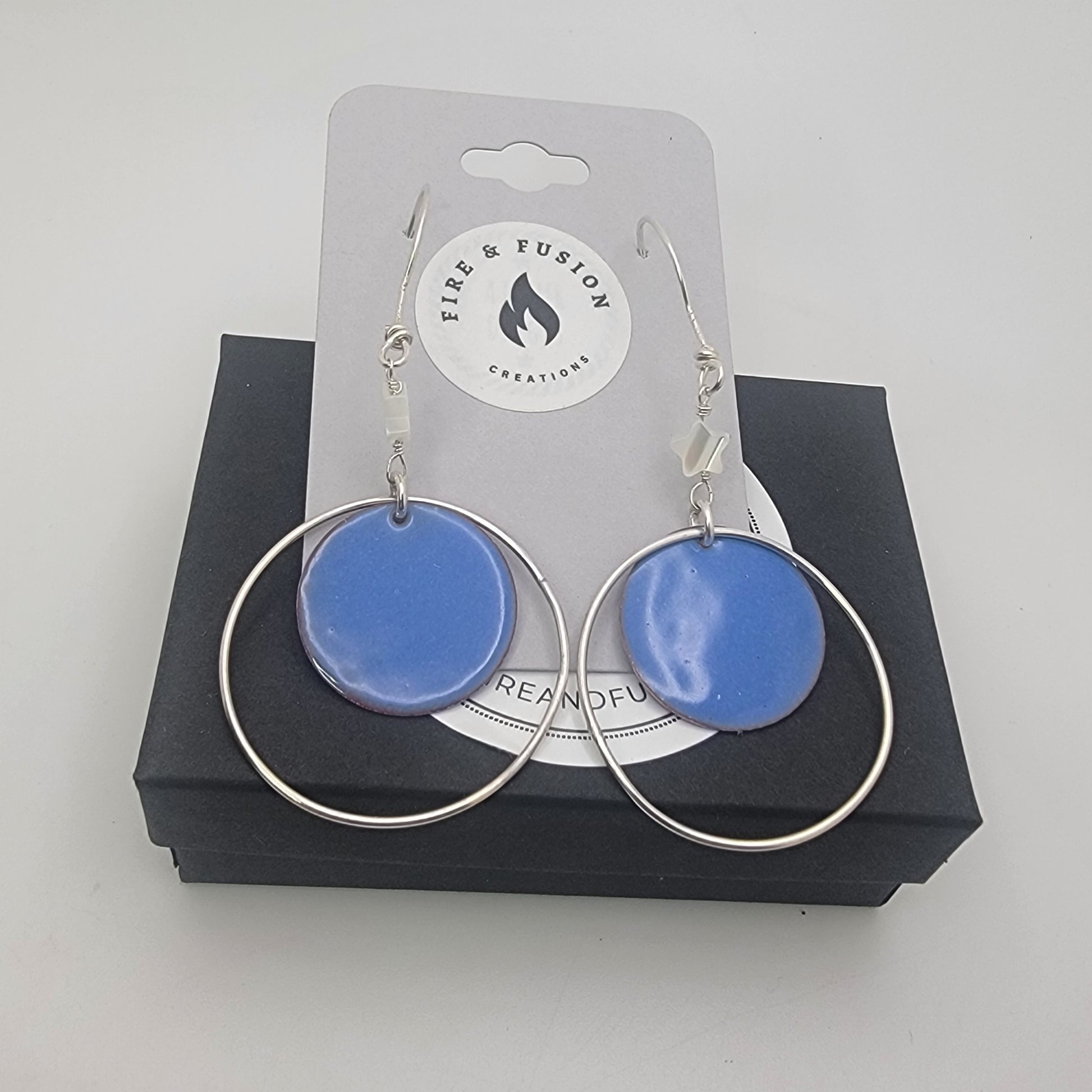 Blue circular earrings with silver loops on a 'Fire & Fusion Creations' card.