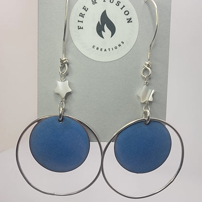Blue circular earrings with silver hoops on jewelry card titled ' Fire and Fusion Creations' against white background