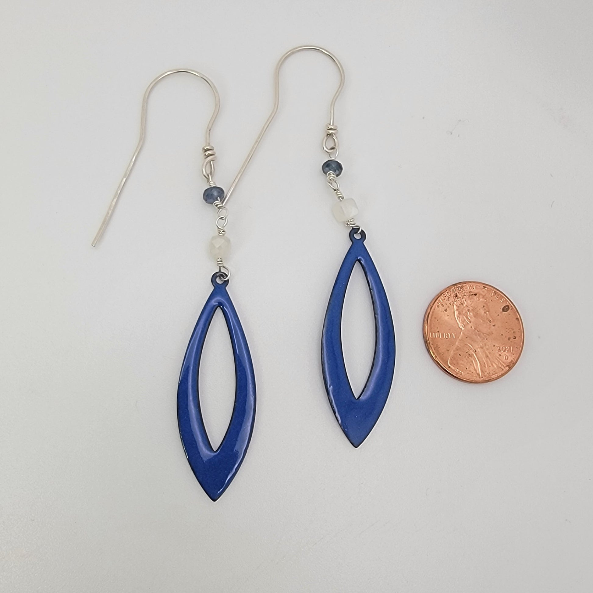 Blue earrings with silver hooks on a white background, next to a penny for scale.