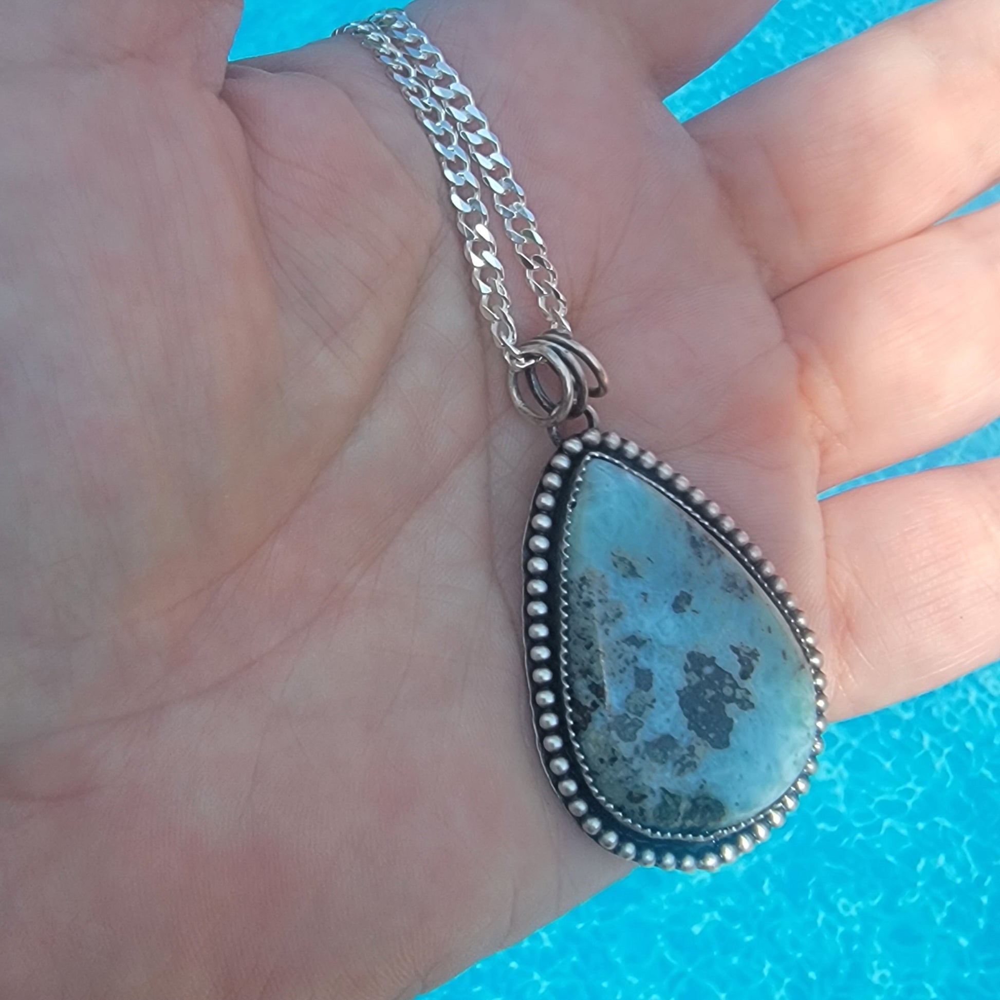 Hand holding blue gemstone pendant in front of water