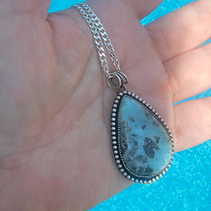 Hand holding blue gemstone pendant in front of water