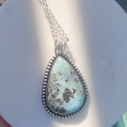 Blue gemstone and bezel set silver pendant on silver curb chain on white background