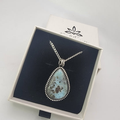 Blue teardop shaped gemstone bezel set pendant shown in branded white gift box on black interior
